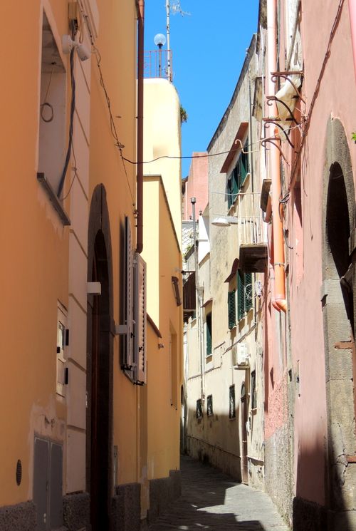 Free Sunlit narrow alley in the historic center of Ischia, showcasing colorful traditional buildings. Stock Photo
