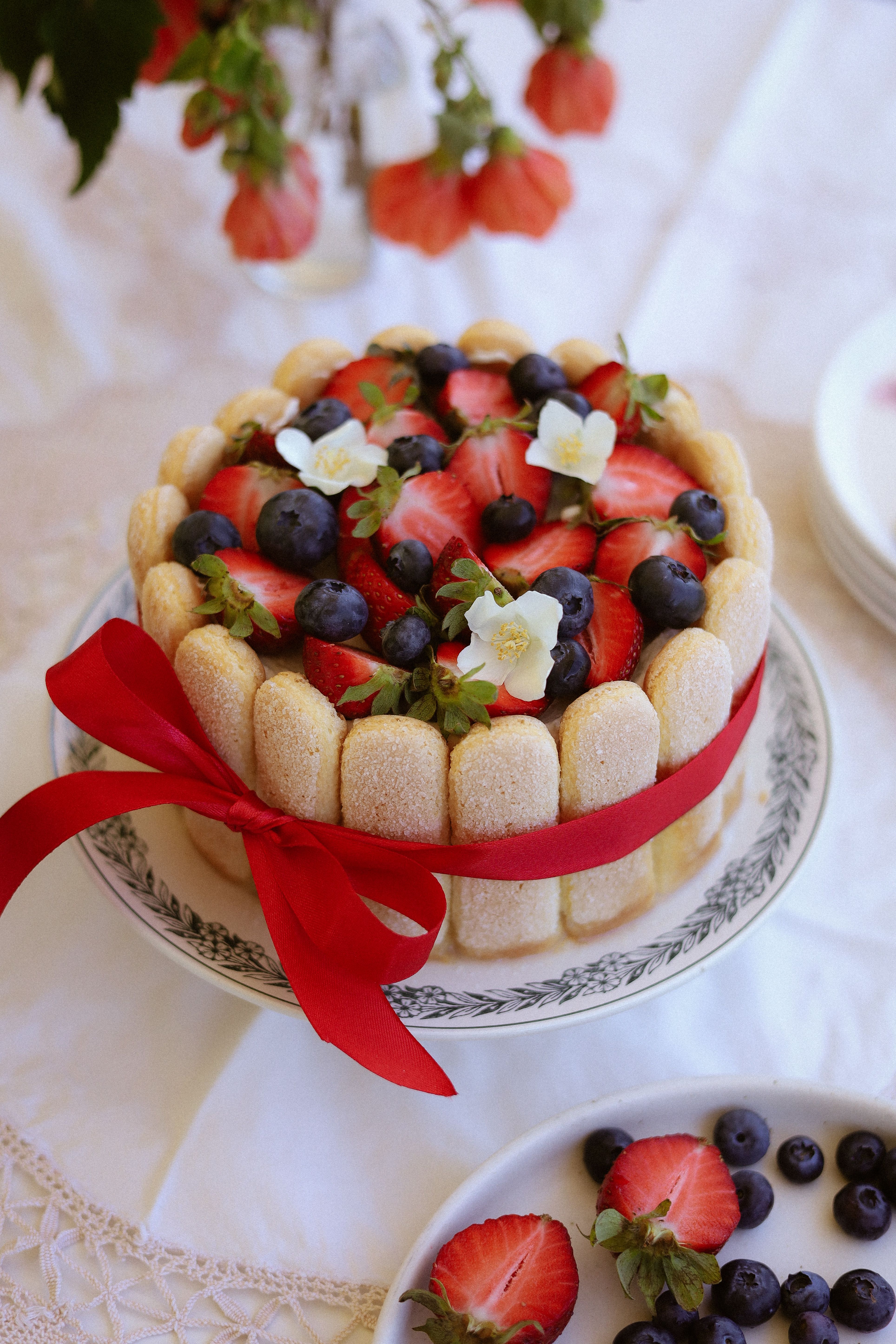 Delightful Charlotte cake adorned with strawberries and blueberries, tied with a red ribbon.