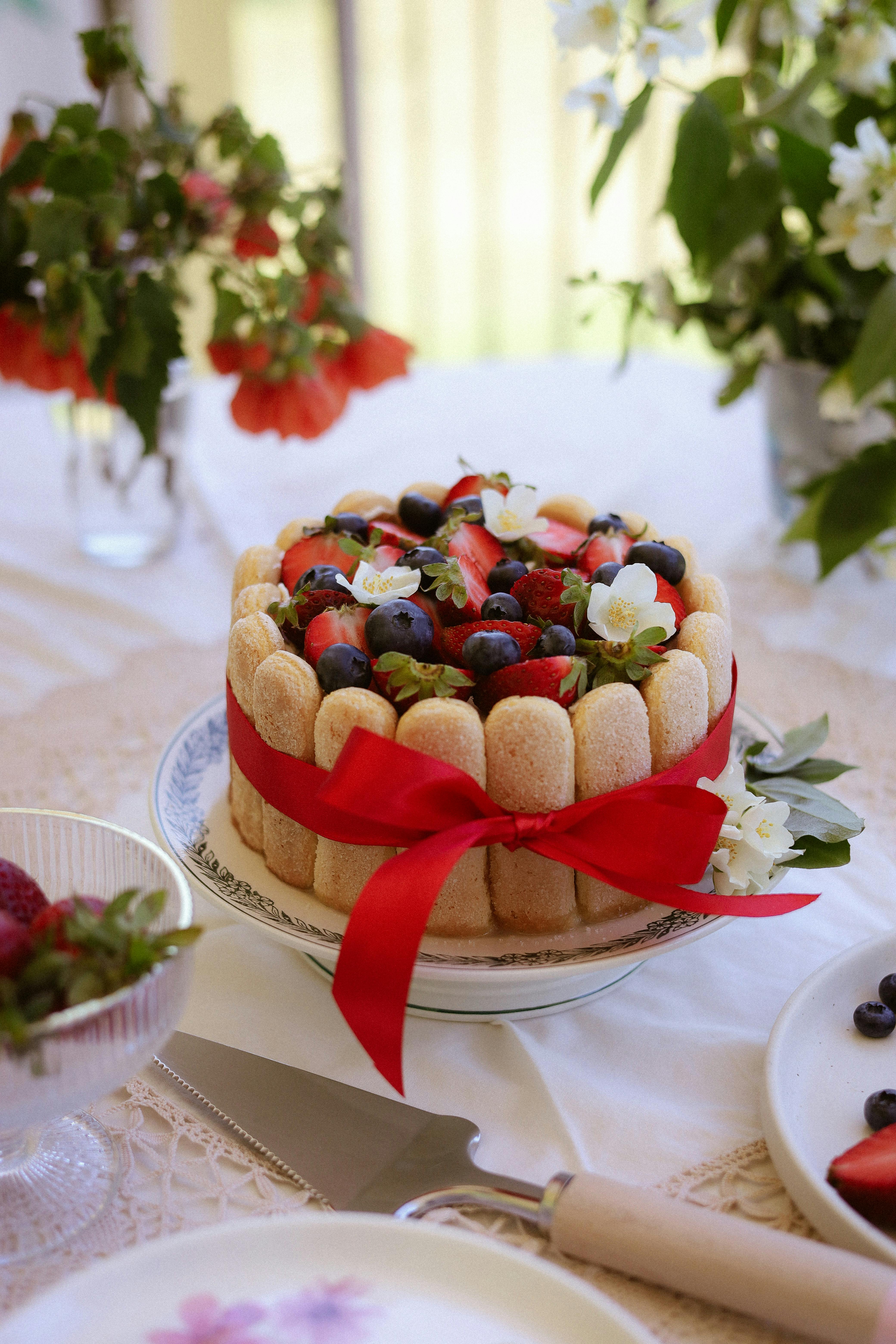Beautiful charlotte cake adorned with berries and flowers on a decorated table setting.