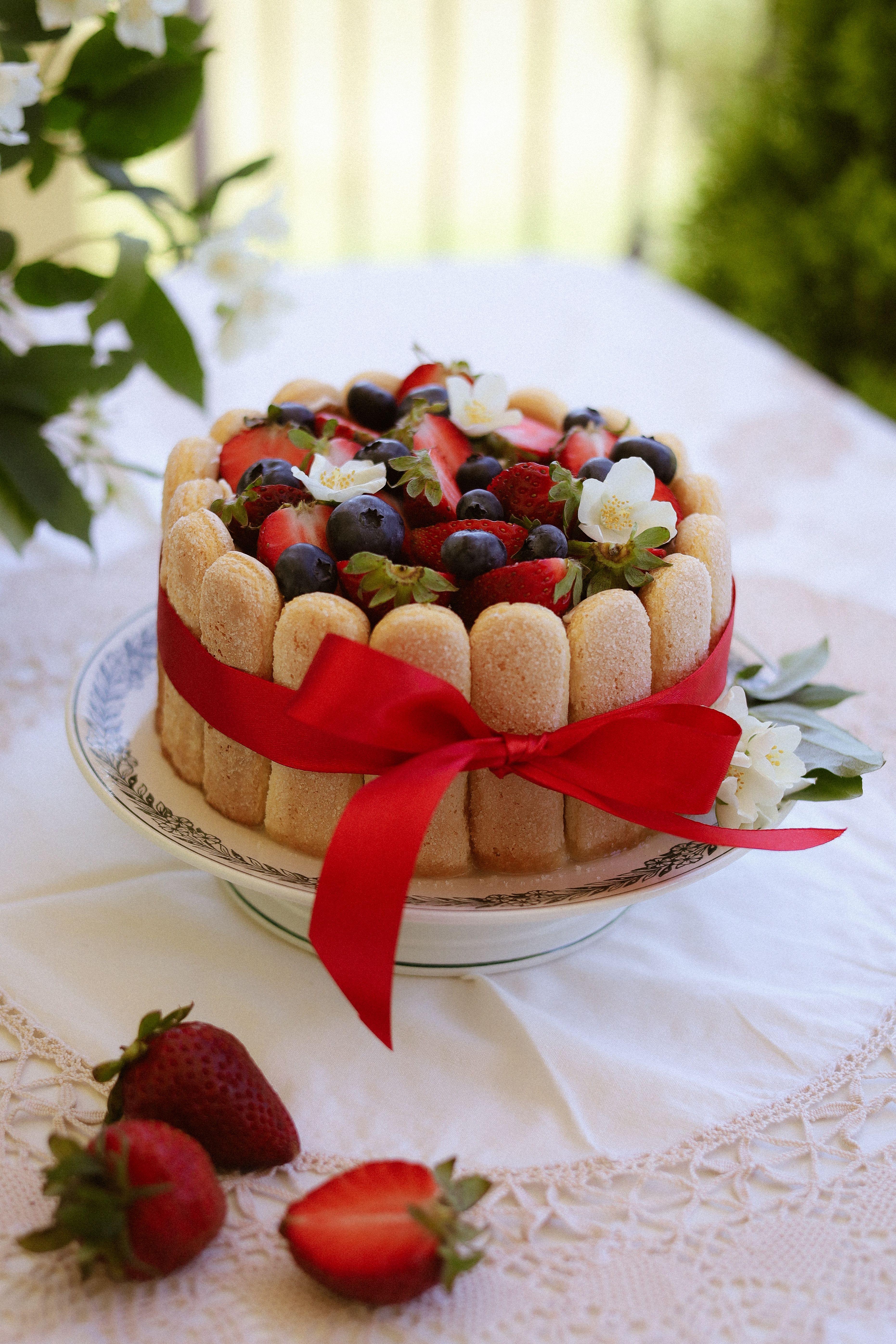A beautifully decorated tiramisu cake topped with fresh strawberries, blueberries, and floral accents.