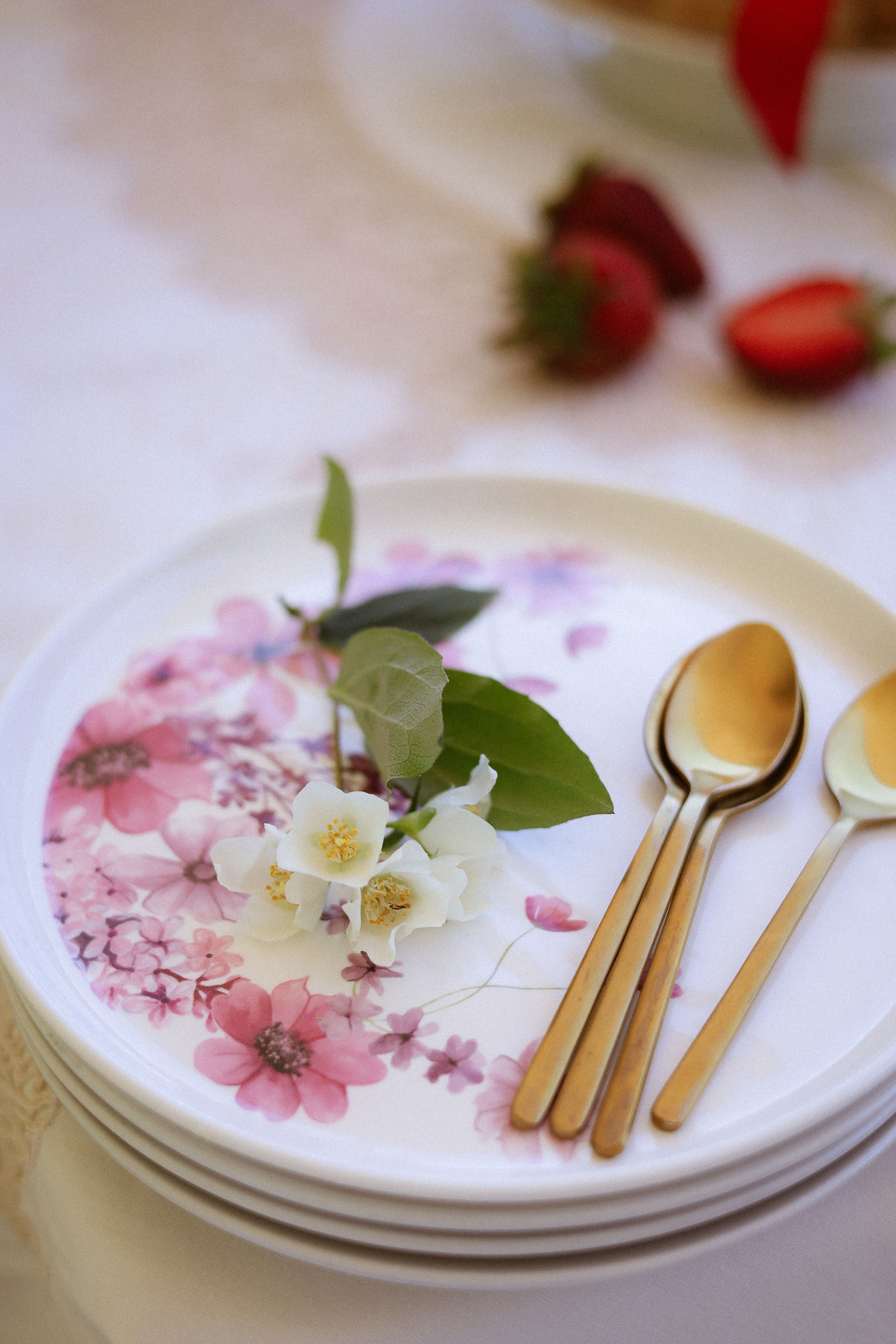 A stylish floral plate setting with gold cutlery and fresh strawberries accentuating the decor.