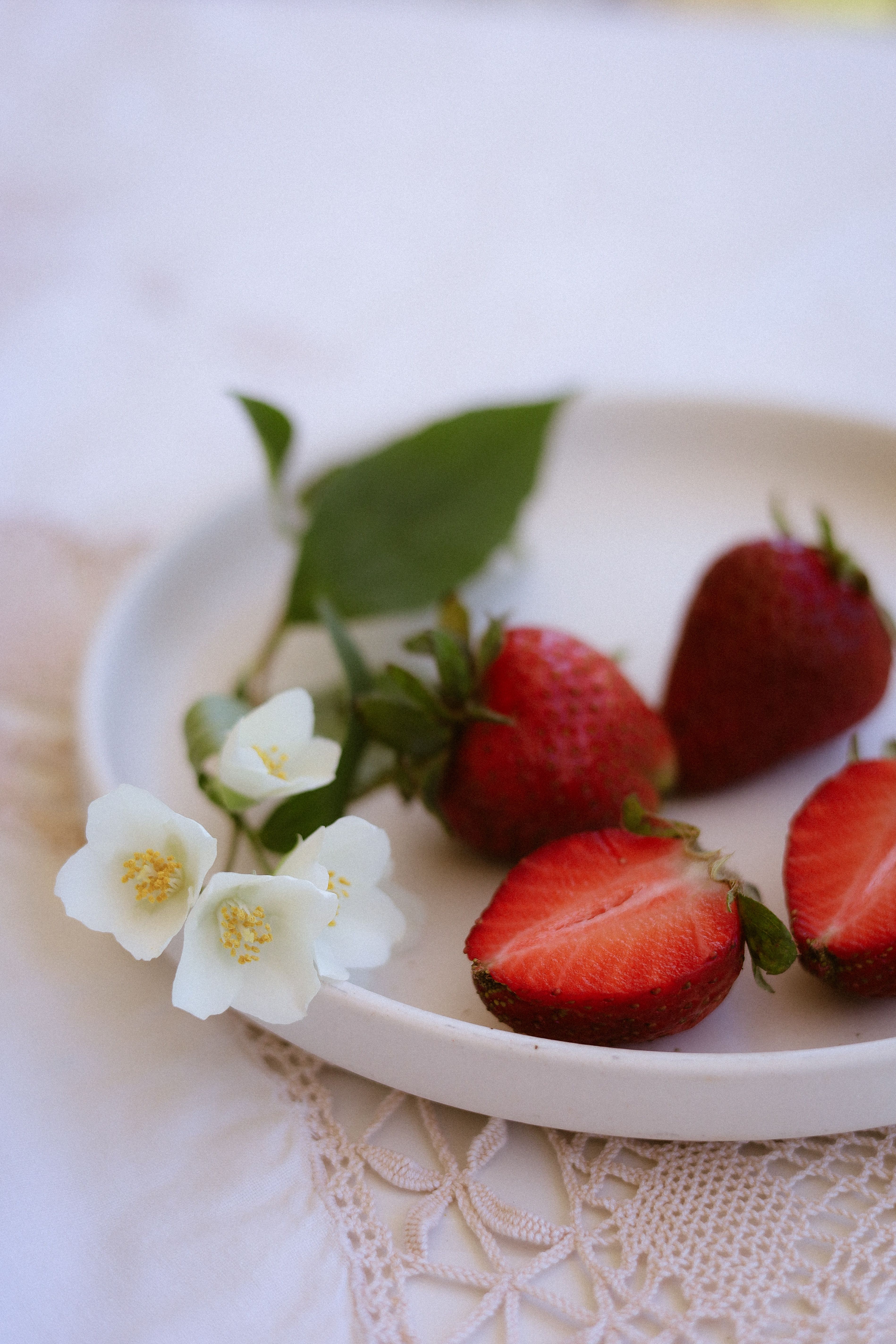 Close-up of fresh strawberries and white flowers on a plate in natural light.