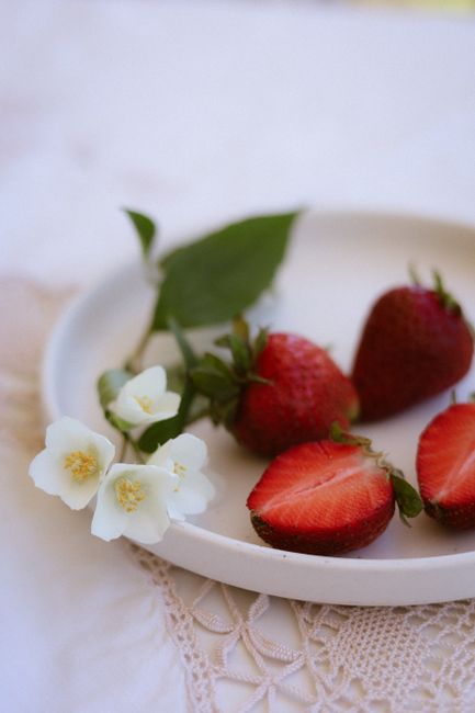 Close-up of fresh strawberries and white flowers on a plate in natural light.