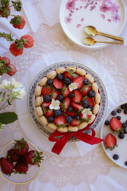 Gourmet cake with strawberries, blueberries, and ladyfingers, elegantly presented on a lace tablecloth.