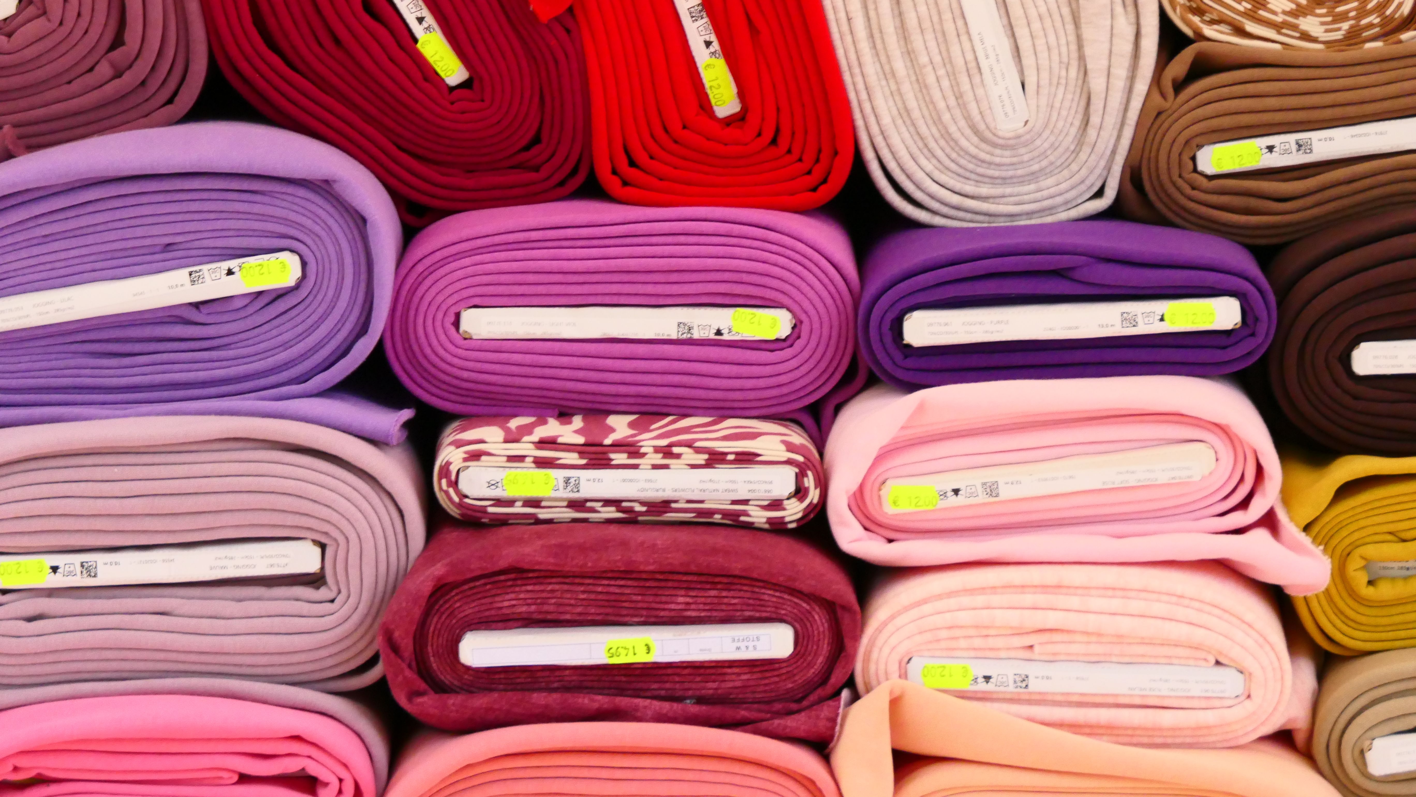 Vibrant fabric rolls in various colors stacked at a Bonn market, perfect for textile projects.