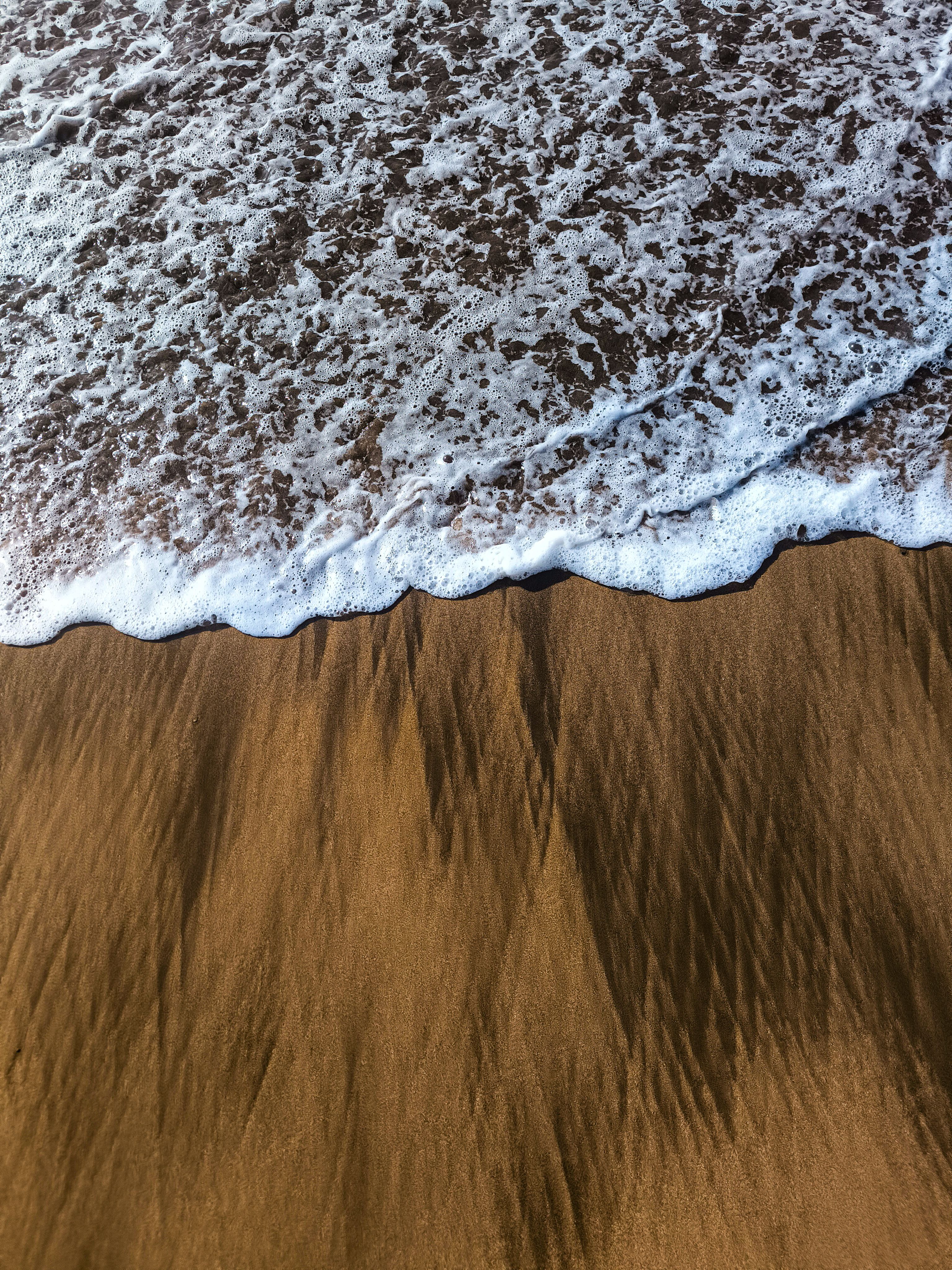 Close-up of a gentle ocean wave caressing a sandy beach, creating a soothing natural pattern.