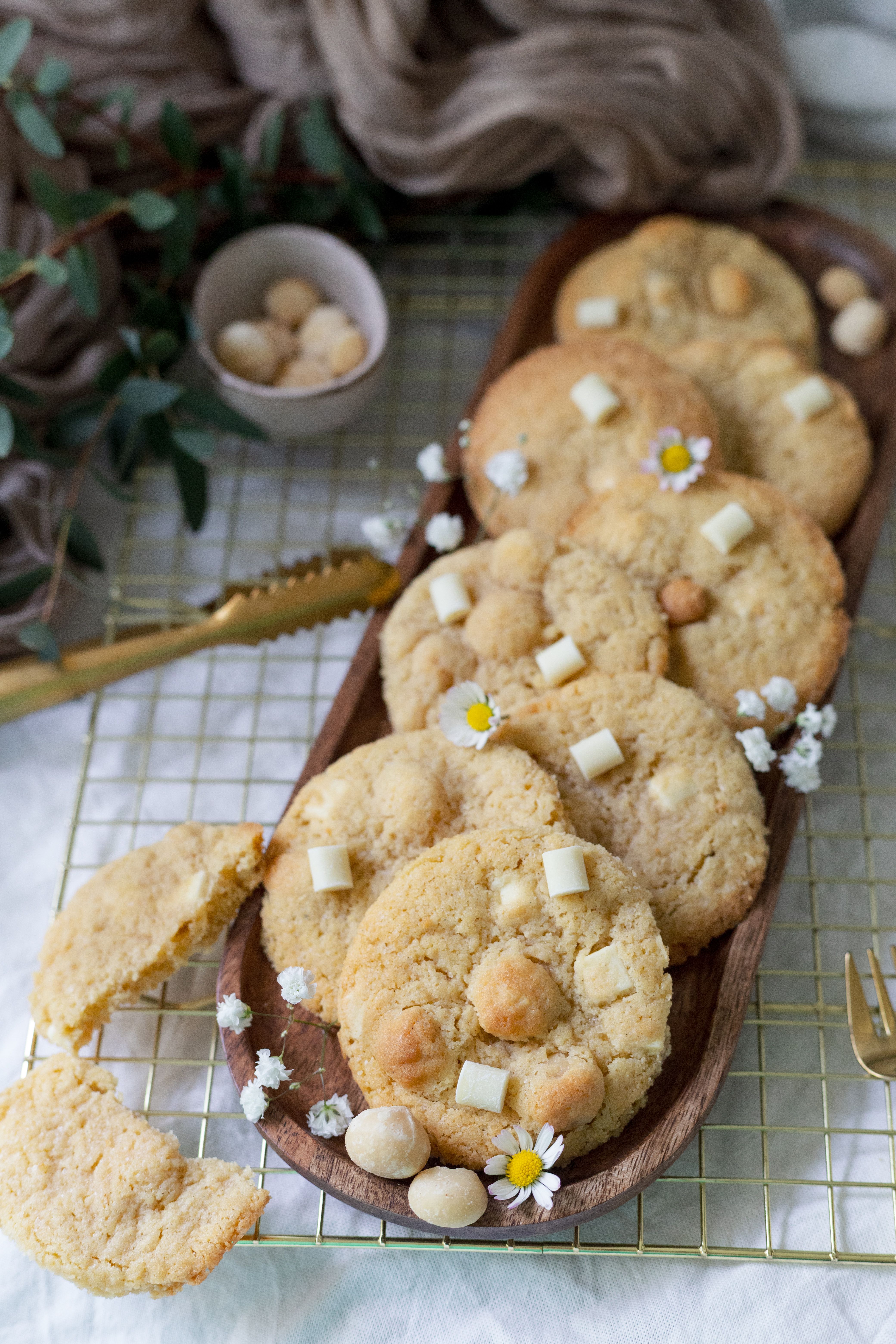 A stack of thick white chocolate macadamia nut cookies with golden-brown edges, melted white chocolate pools, and chopped macadamia nuts visible on top, on a cooling rack.