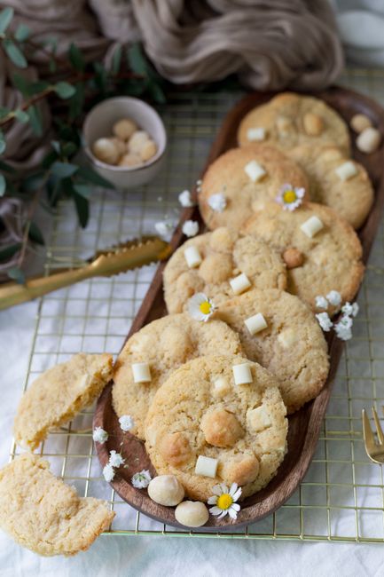 A stack of thick white chocolate macadamia nut cookies with golden-brown edges, melted white chocolate pools, and chopped macadamia nuts visible on top, on a cooling rack.
