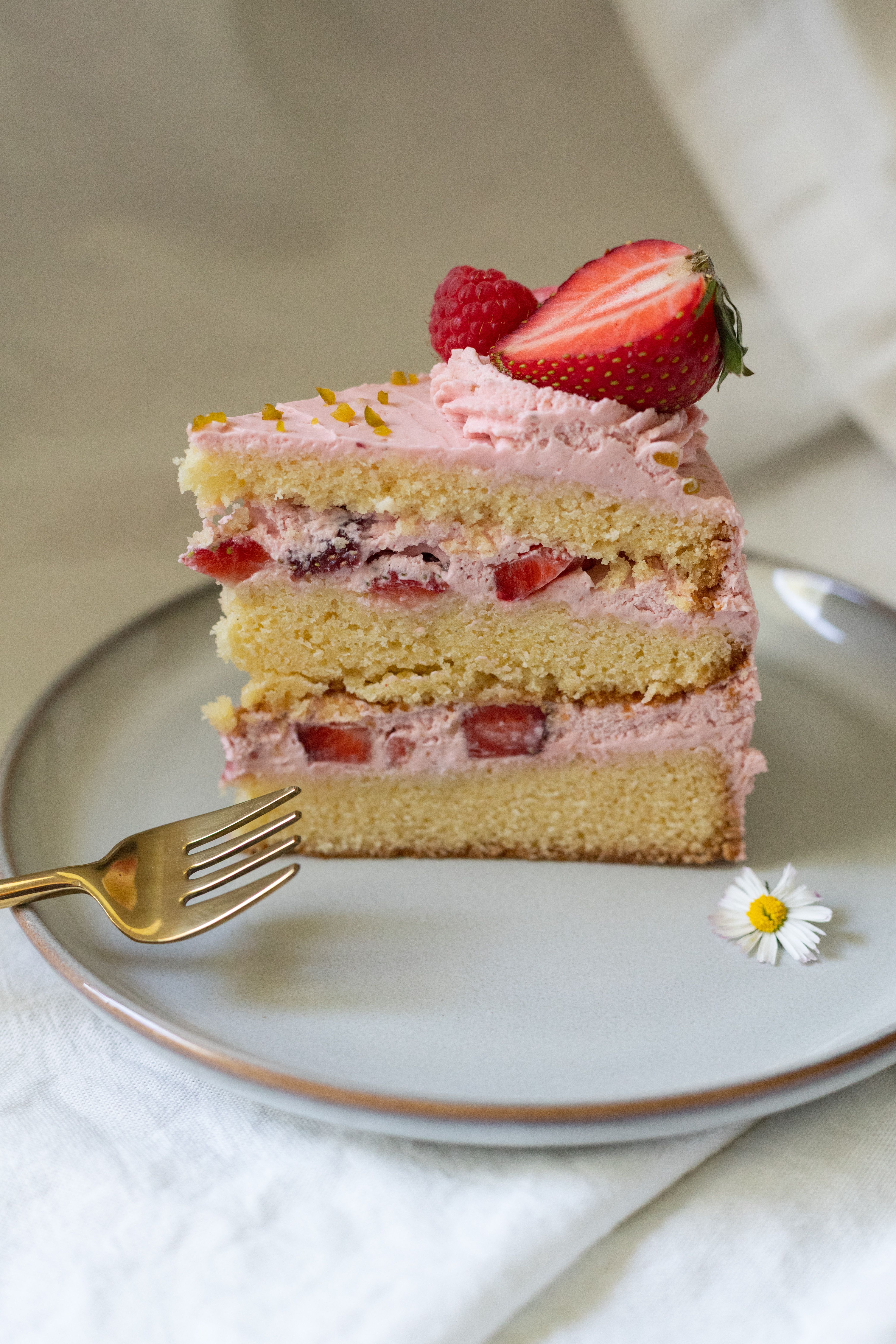 A mouth-watering slice of strawberry layer cake with pink frosting and berries, styled on a ceramic plate.
