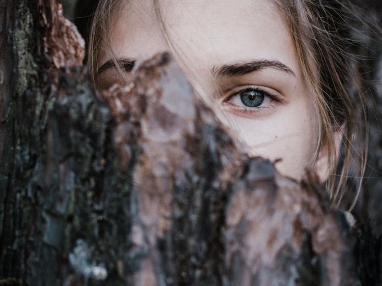 Calm Woman Behind Tree Bark In Park