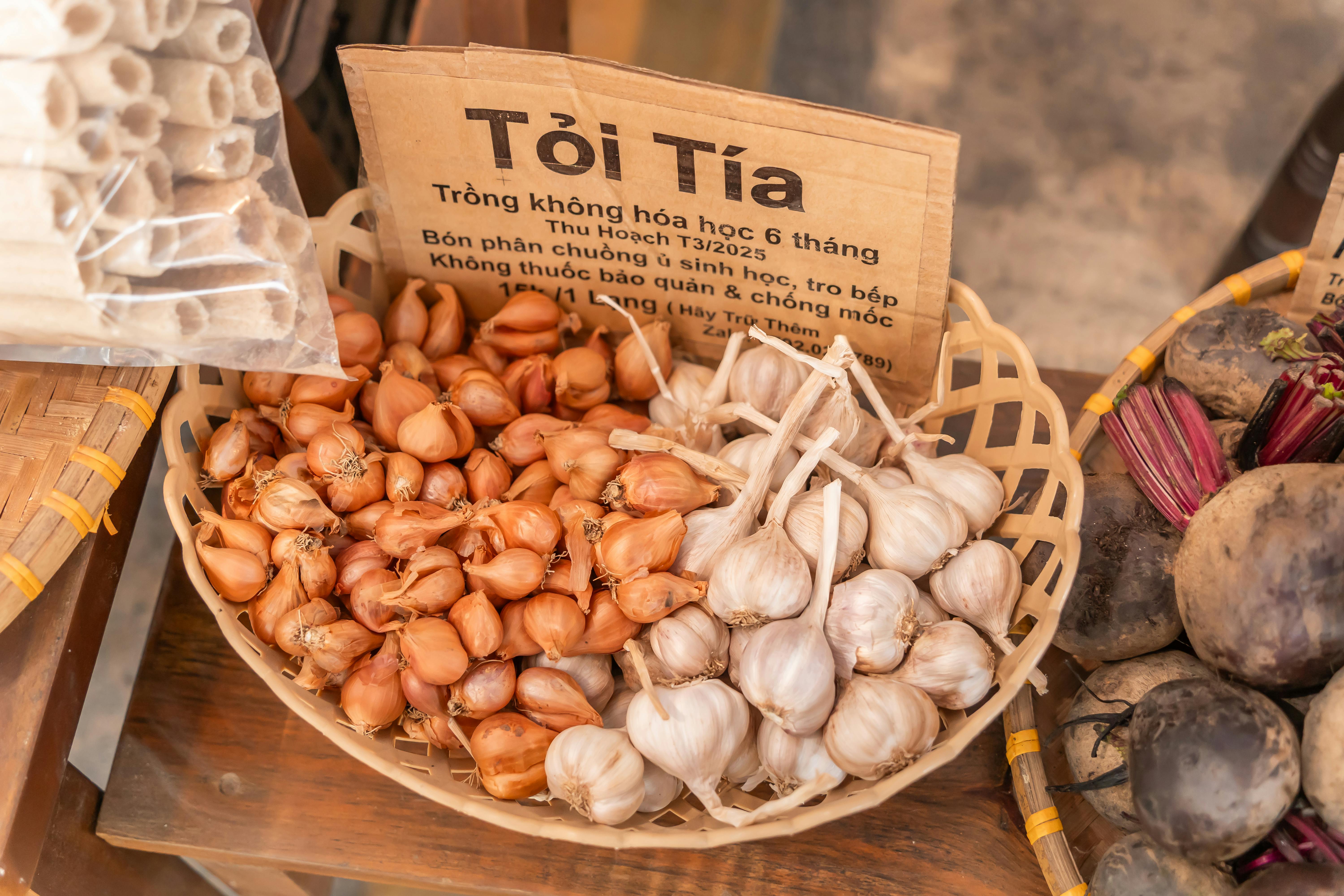 A basket of organic garlic and shallots on display at a market stall, showcasing fresh produce.