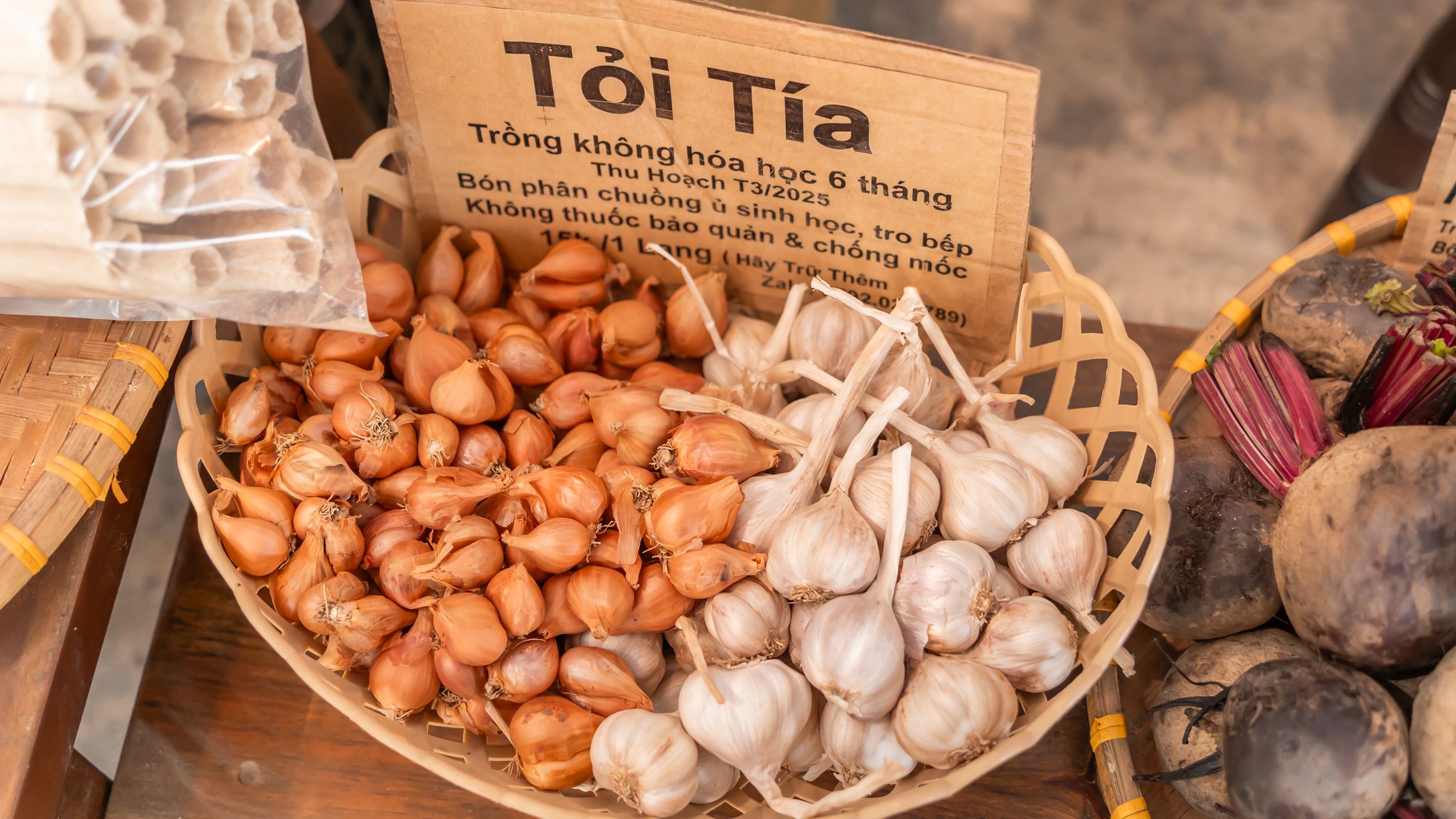 A basket of organic garlic and shallots on display at a market stall, showcasing fresh produce.