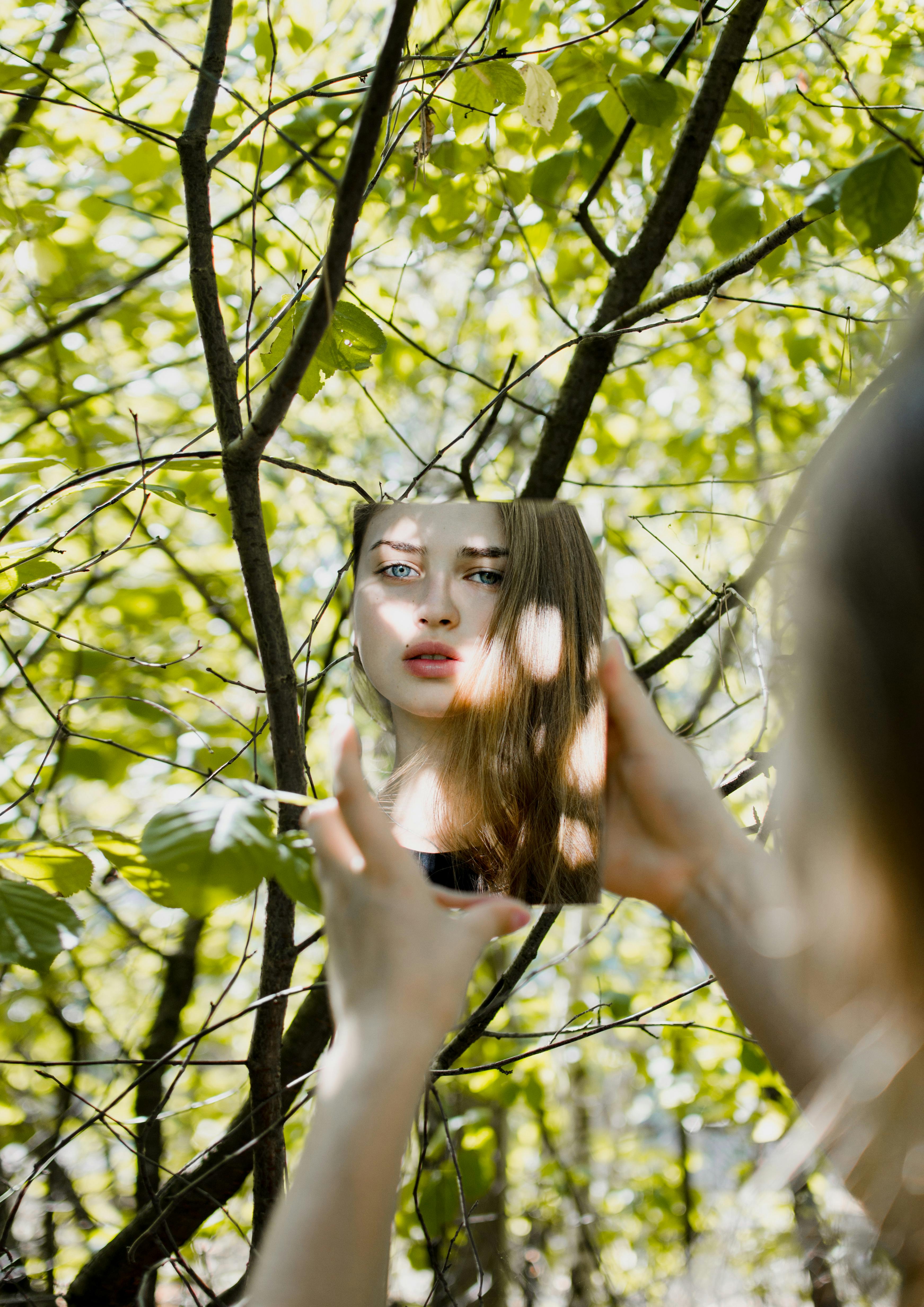 一名女子凝视着镜子，镜面被鲜艳的绿叶环绕，映出一幅梦幻般的肖像