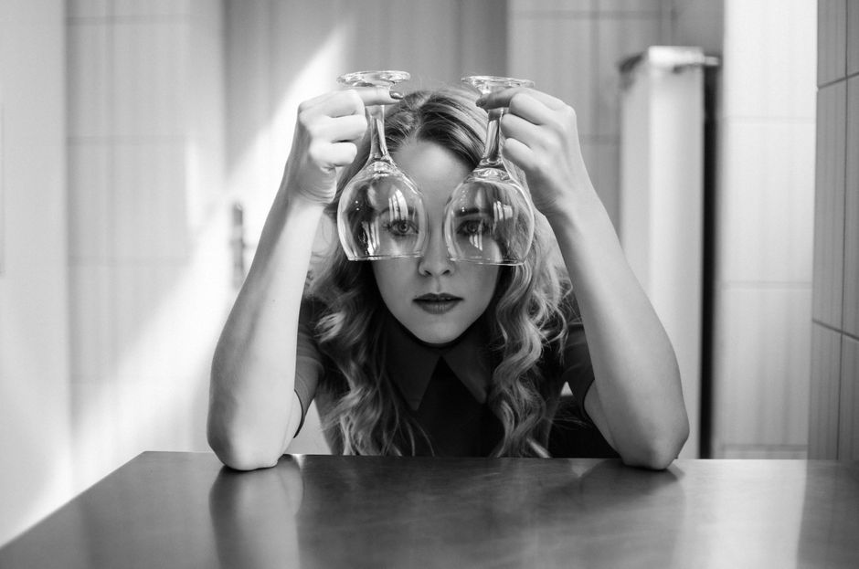 Creative black and white portrait of a woman holding two wine glasses, creating a unique artistic effect.