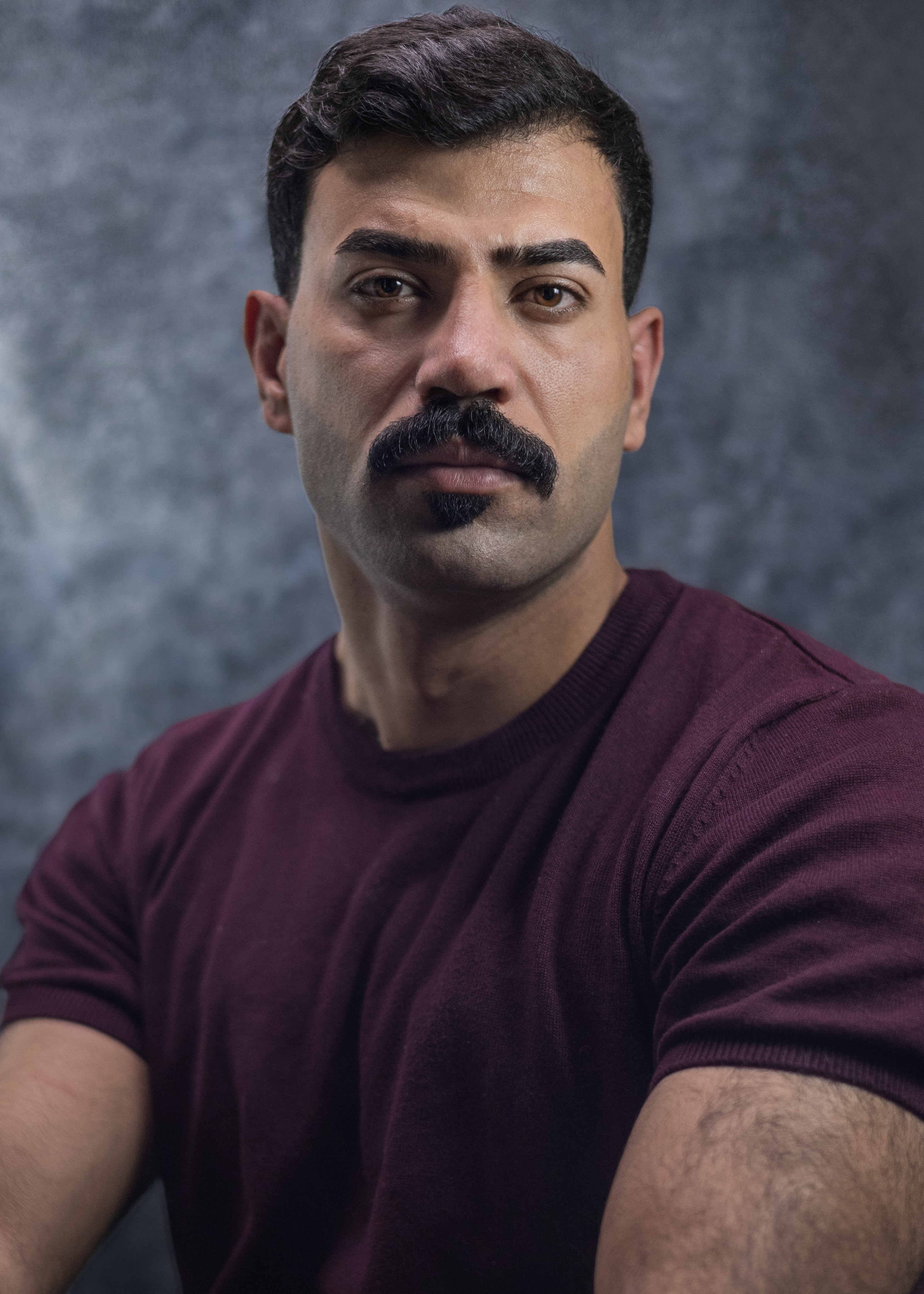 Close-up portrait of a serious man with a mustache in a dark shirt.