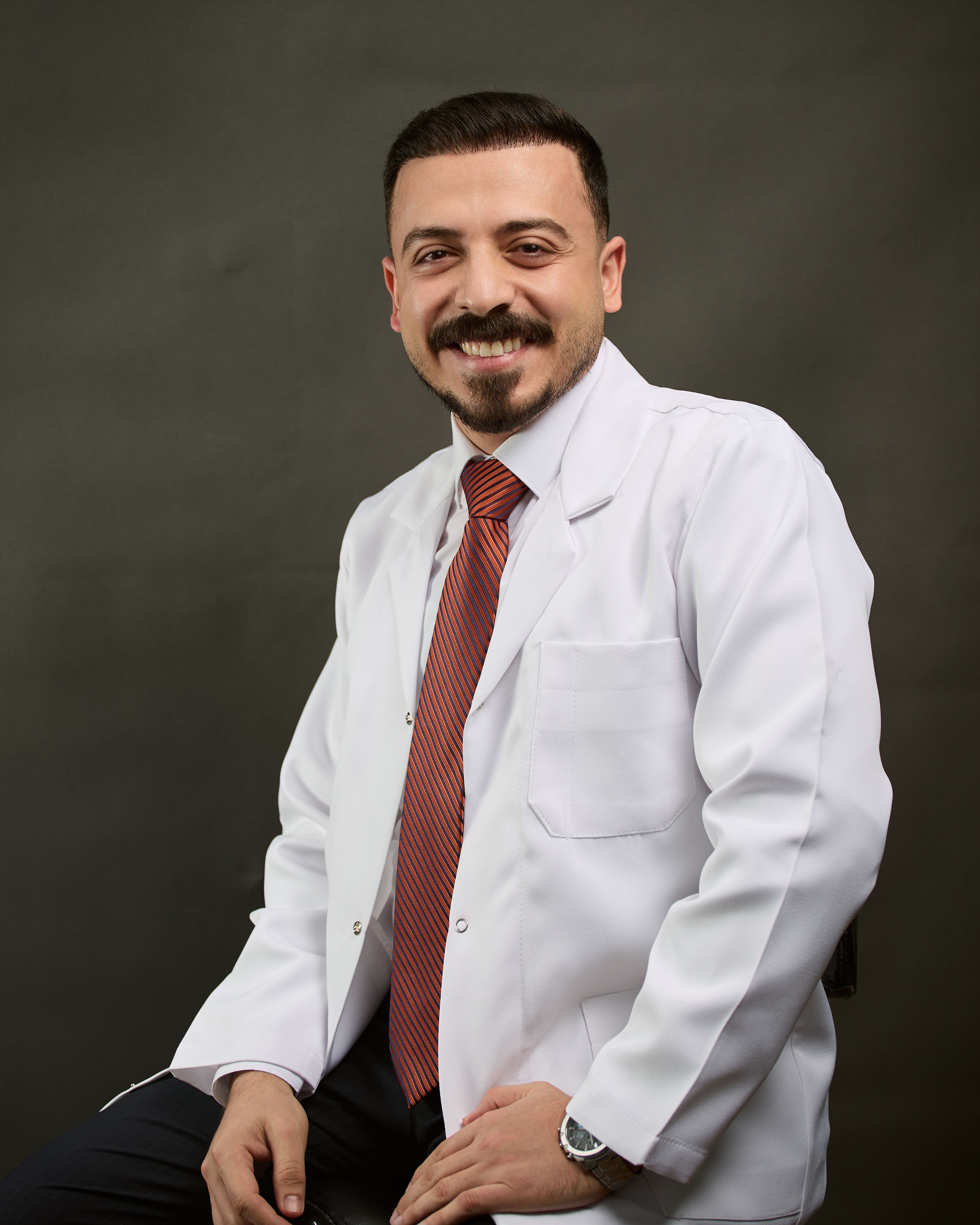 Confident male doctor in white coat smiling warmly in a studio setting.