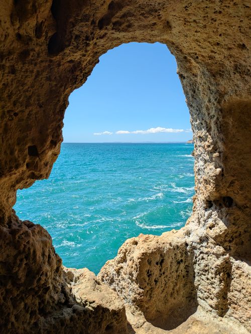 Free View of the Algarve's stunning blue ocean through a natural rock cave frame in Faro District, Portugal. Stock Photo