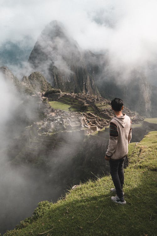 A person standing on a mountain overlooking the ancient structure of Machu Picchu
