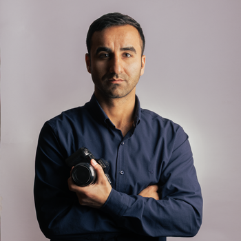 Professional photographer posing with a camera against a gray background.
