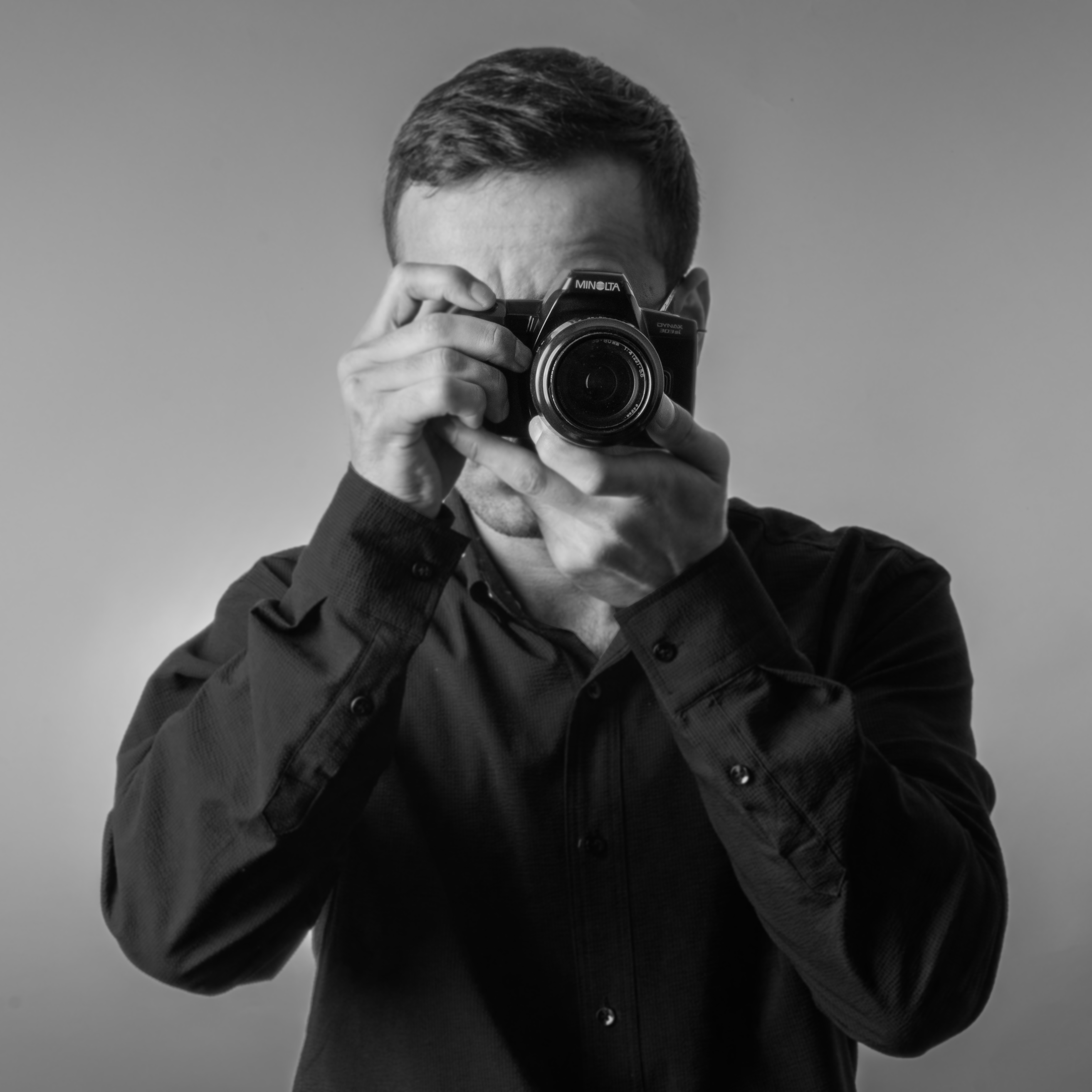 Black and white portrait of a man photographing with a vintage camera.