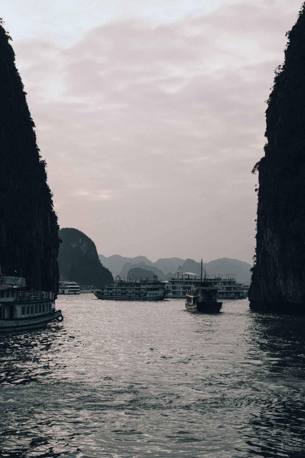 Cruise boats beneath tall limestone cliffs in soft evening light