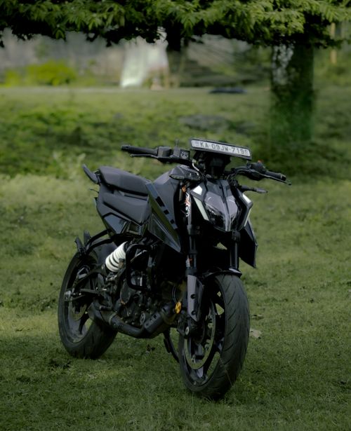 Free A sleek black motorcycle parked outdoors, showcasing its stylish design against a green backdrop. Stock Photo