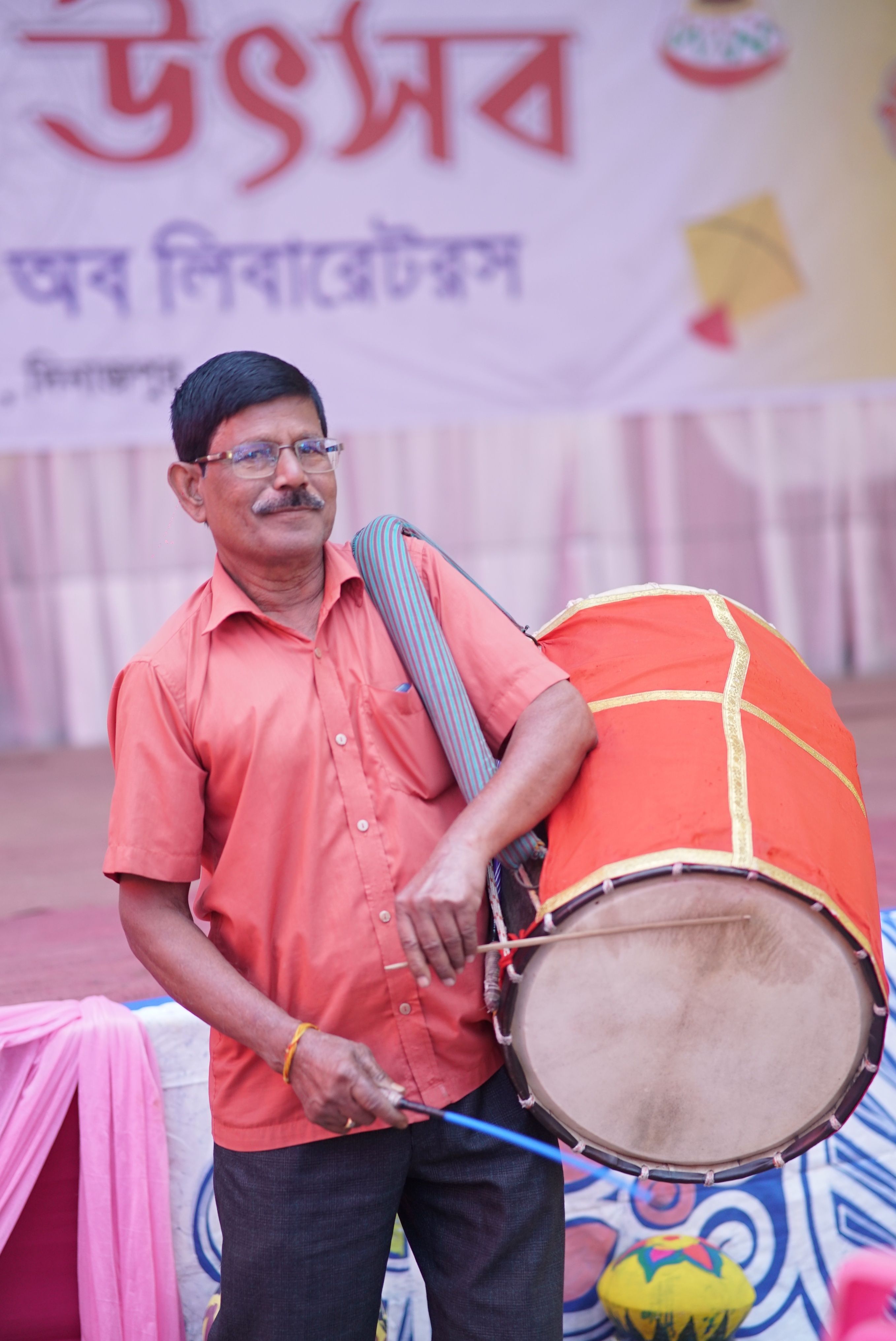 A man in a red shirt playing a vibrant traditional drum at a cultural festival.