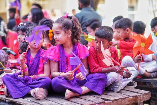 Group of children in colorful attire holding pinwheels at a lively festival.