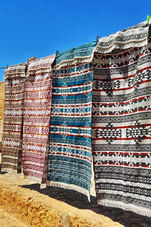 Free Vibrant traditional rugs displayed against a clear blue sky, showcasing intricate patterns and colors. Stock Photo