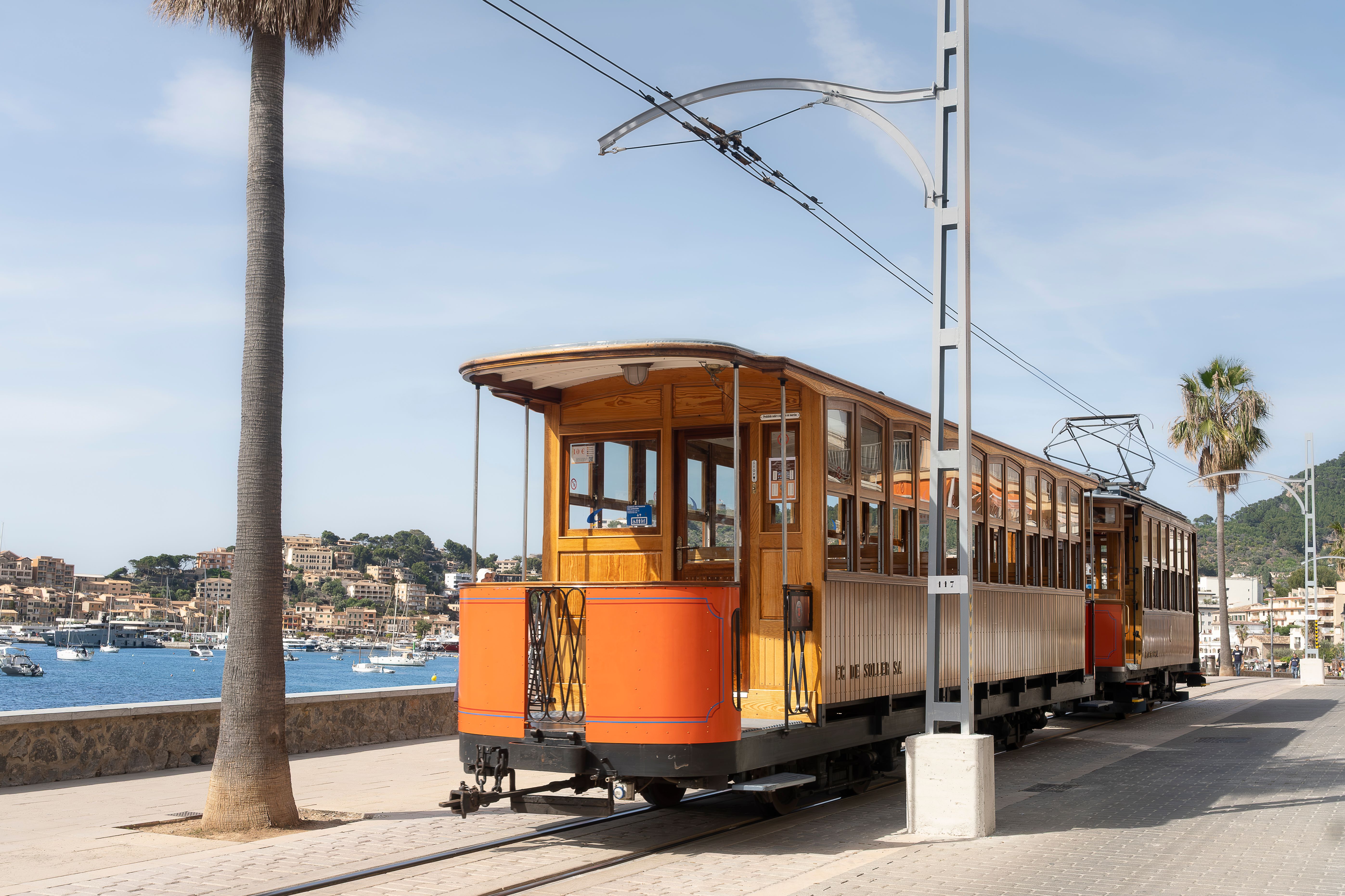 A vintage orange wooden tram beside palm trees at Port de Soller