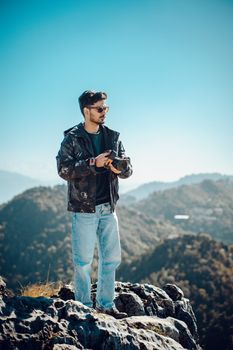 Young man stands on a rocky mountaintop, taking in a serene and scenic view of the mountains.