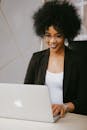 在现代办公环境中，一位留着非洲发型的女性面带微笑，正用笔记本电脑工作