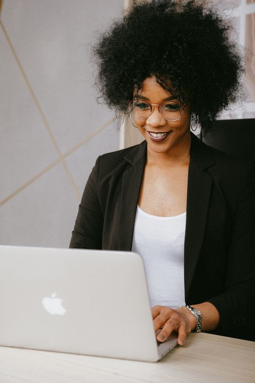 Free Smiling woman with afro hair working on a laptop in a modern office setting. Stock Photo