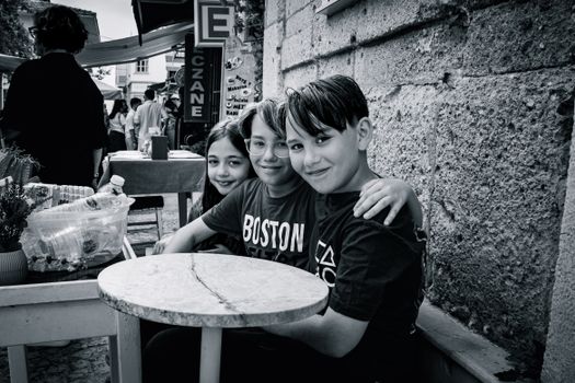 Three smiling children sitting at an outdoor cafe table, enjoying each other's company.