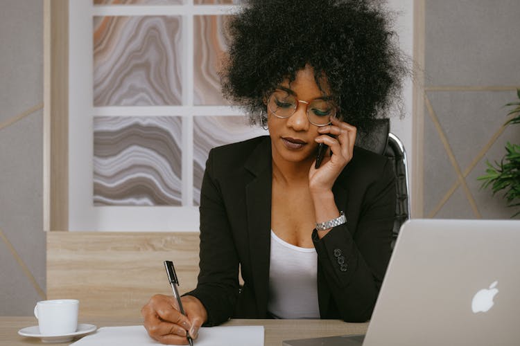 woman using a mobile device while writing in a notebook