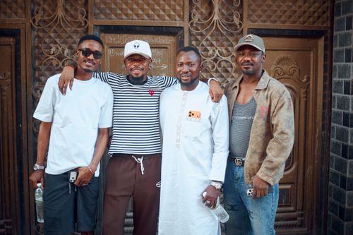 Free Group of four men posing happily in casual attire against an ornate door background. Stock Photo