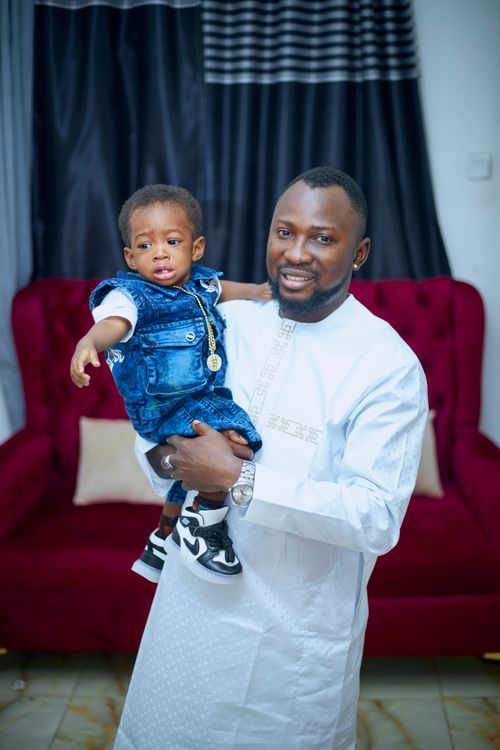 Free Father holds his young son dressed in denim overalls indoors, on a red couch background. Stock Photo