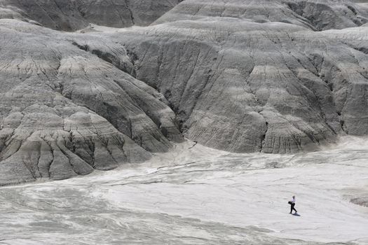 A lone hiker walks across a gray, barren rocky landscape, depicting isolation and nature's vastness.
