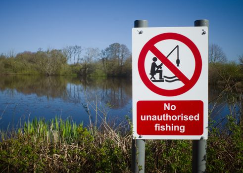 A clear no fishing sign by a serene lake under a bright blue sky, emphasizing nature preservation.