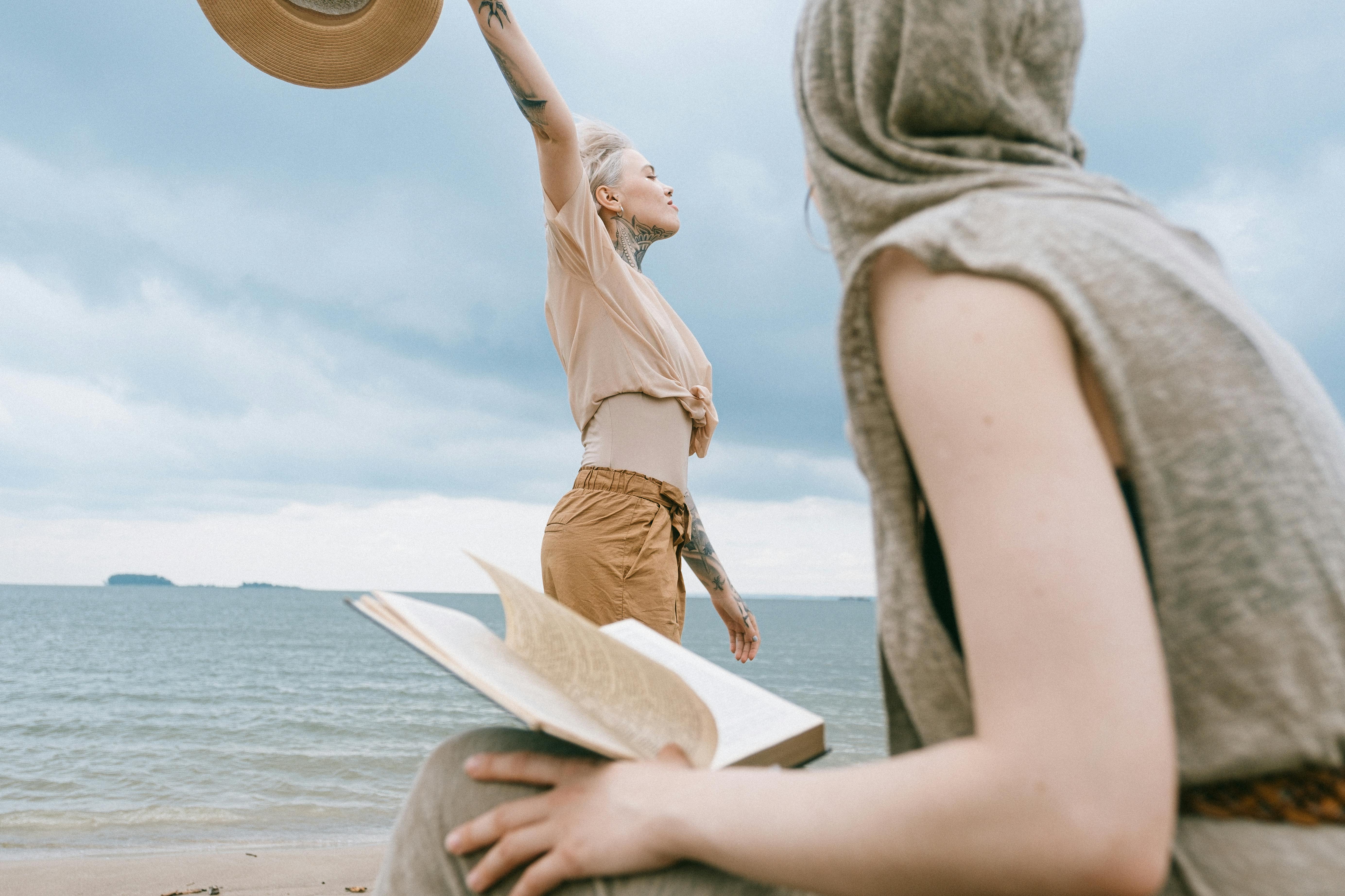 两个女人在海滩上享受休闲时光，一个在阅读，另一个在拥抱自由