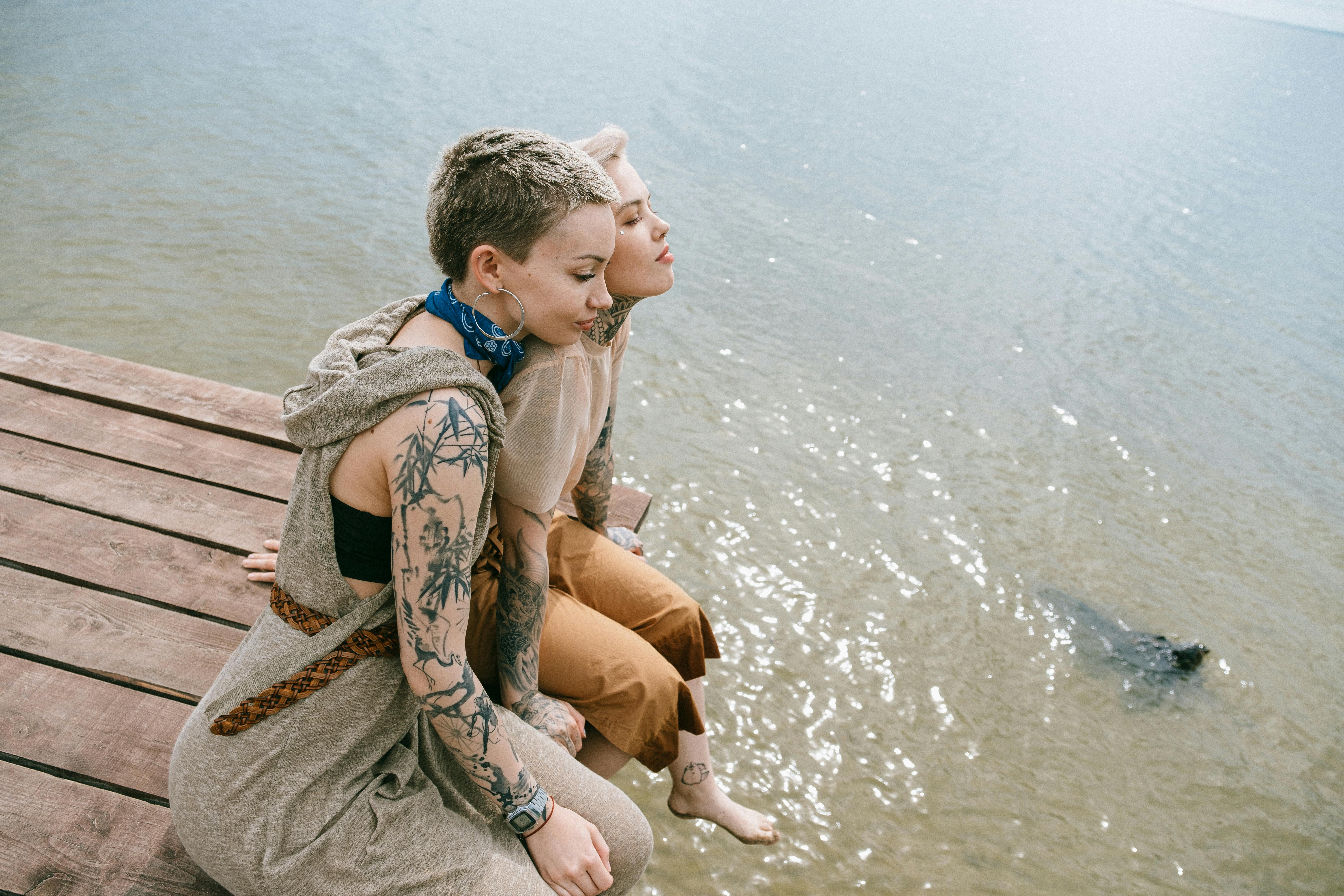 两名纹身女子坐在码头上，享受着阳光明媚的海滨时光