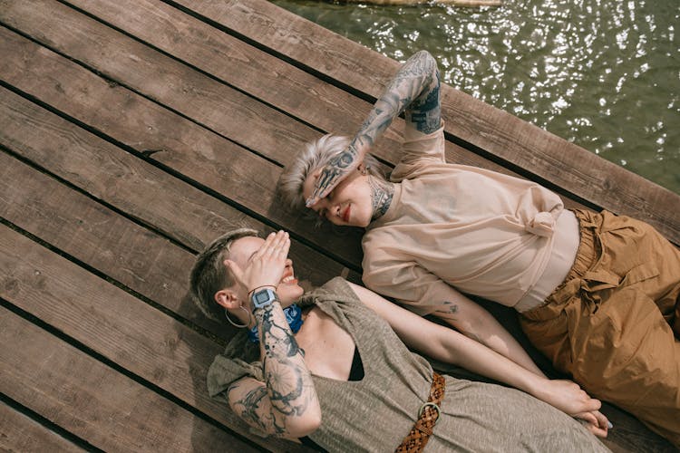 High Angle Photo Of Women Lying Down On Wooden Planks While Covering Their Face