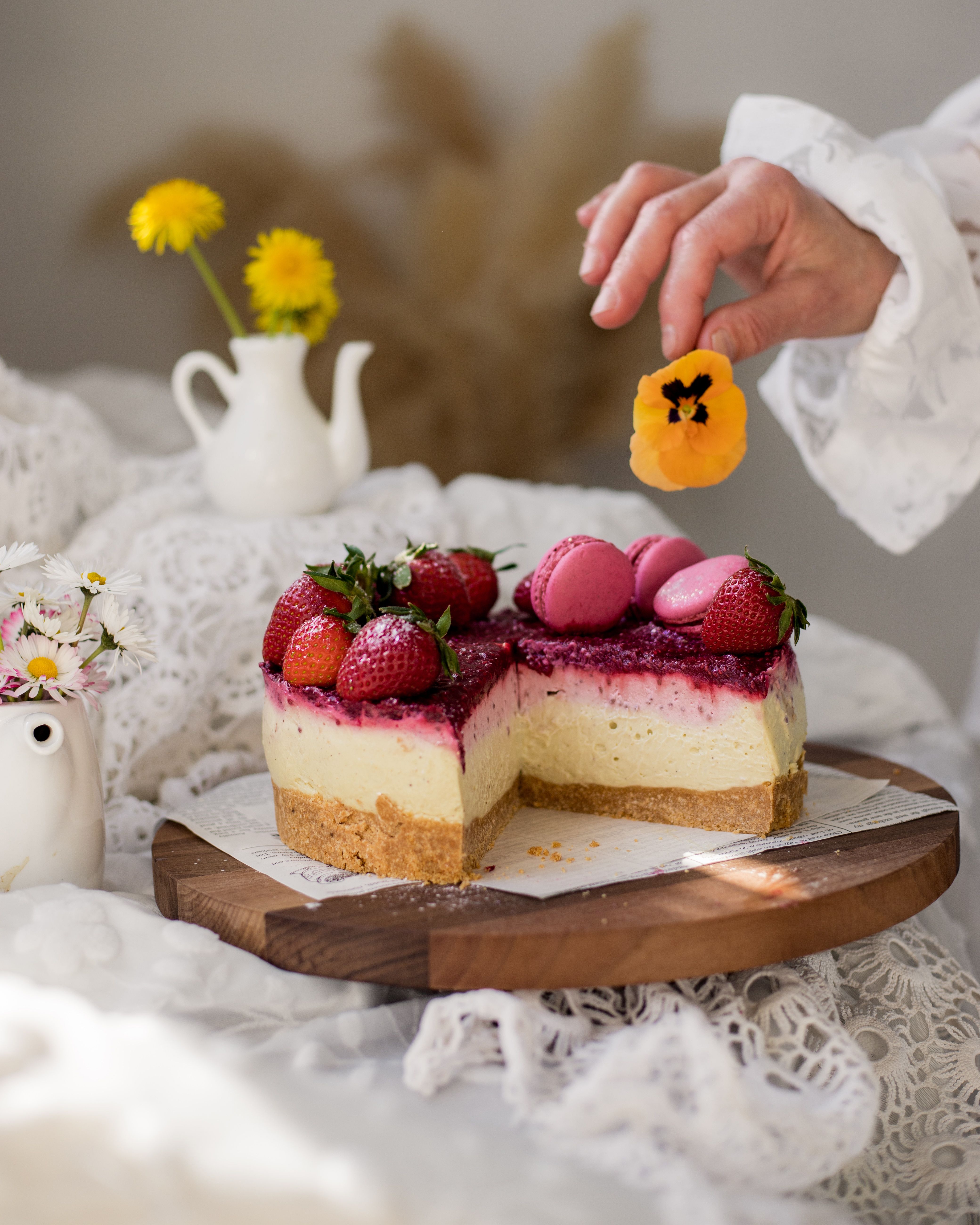 Elegant homemade strawberry cheesecake with hand garnish and fresh flowers, perfect for summer occasions.