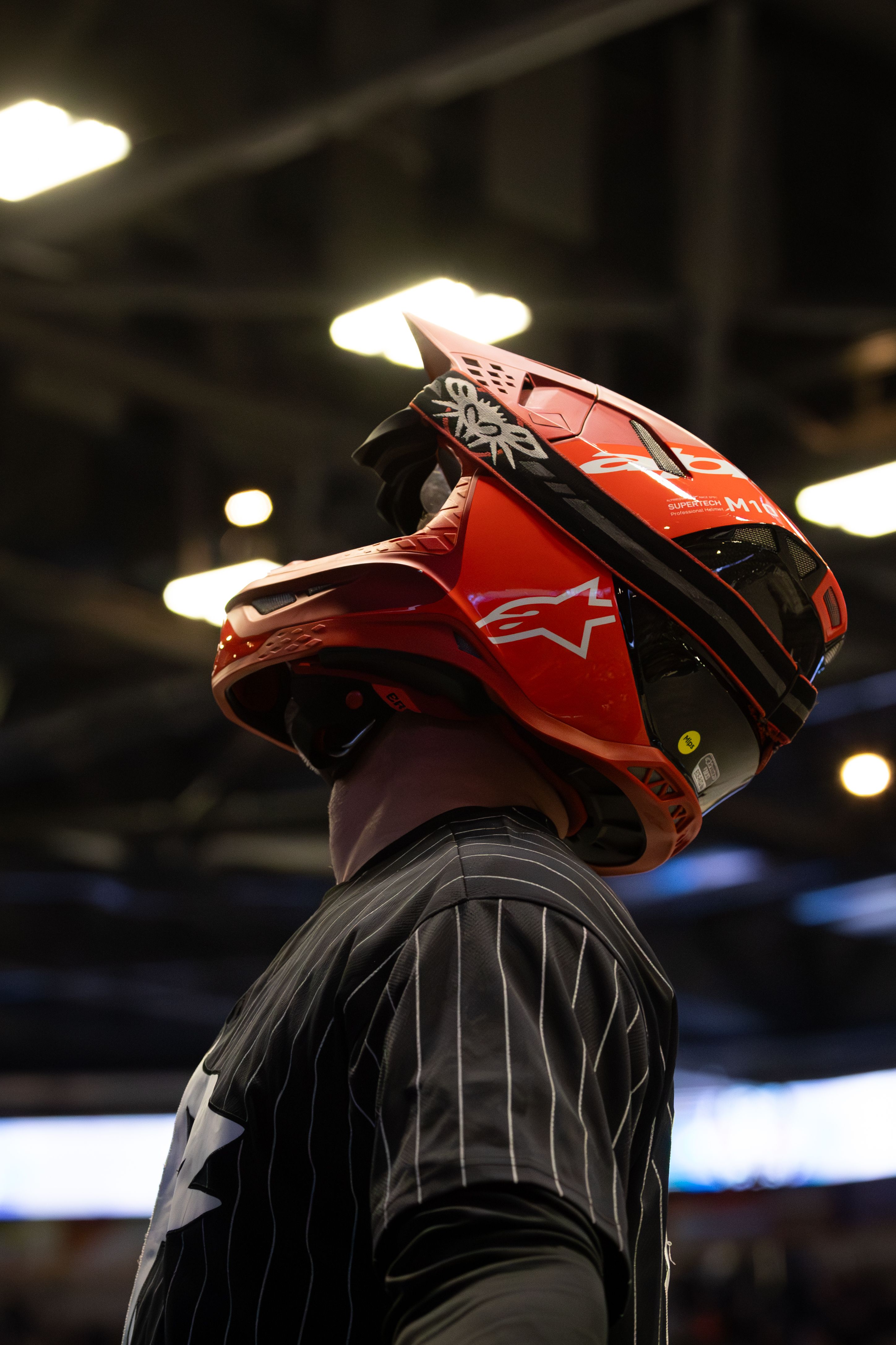 Motocross rider wearing a red helmet indoors with dramatic lighting.