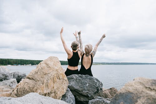 Free Women Sitting on Rock While Raising Their Hands Stock Photo