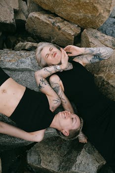 两个女人躺在岩石上，身上有纹身，享受着户外的乐趣