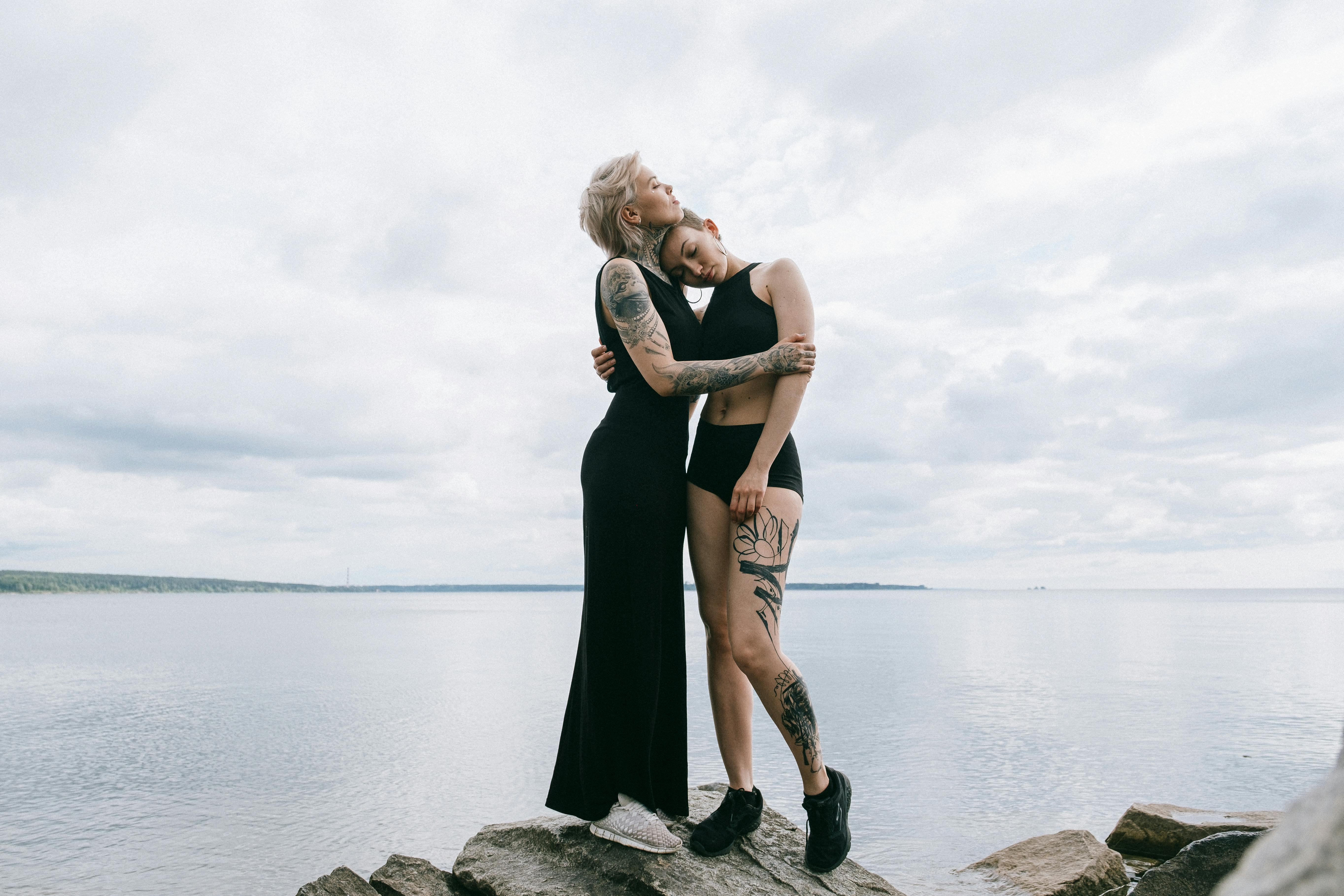 woman in black tank dress standing on rock near body of water