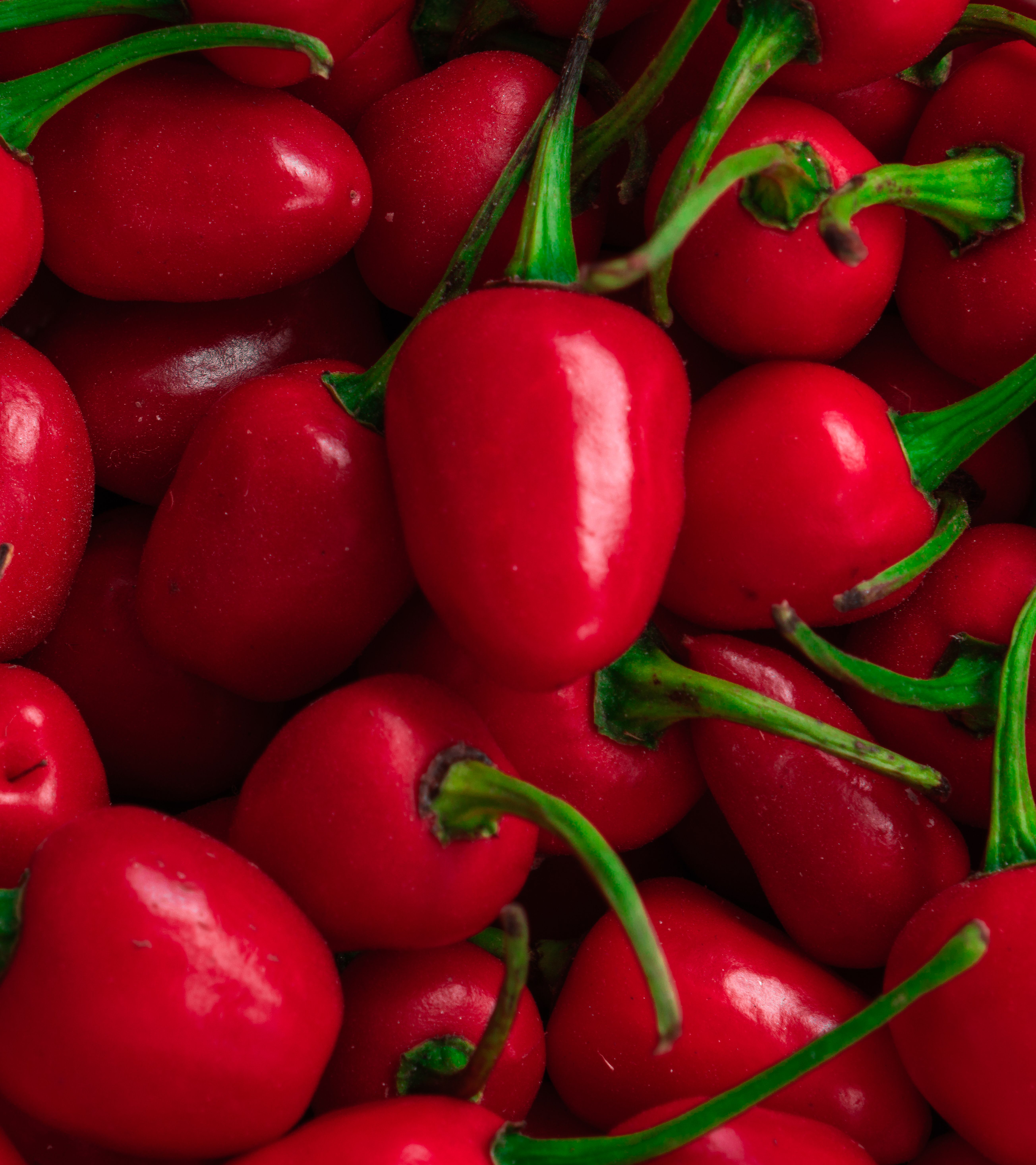 A pile of round red and green cherry peppers, some whole and one sliced open showing the thick white ribs and seeds inside