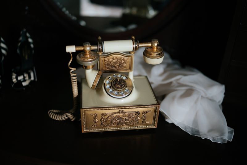 Antique rotary telephone with ornate gold details, displayed indoors with a classic decorative style.