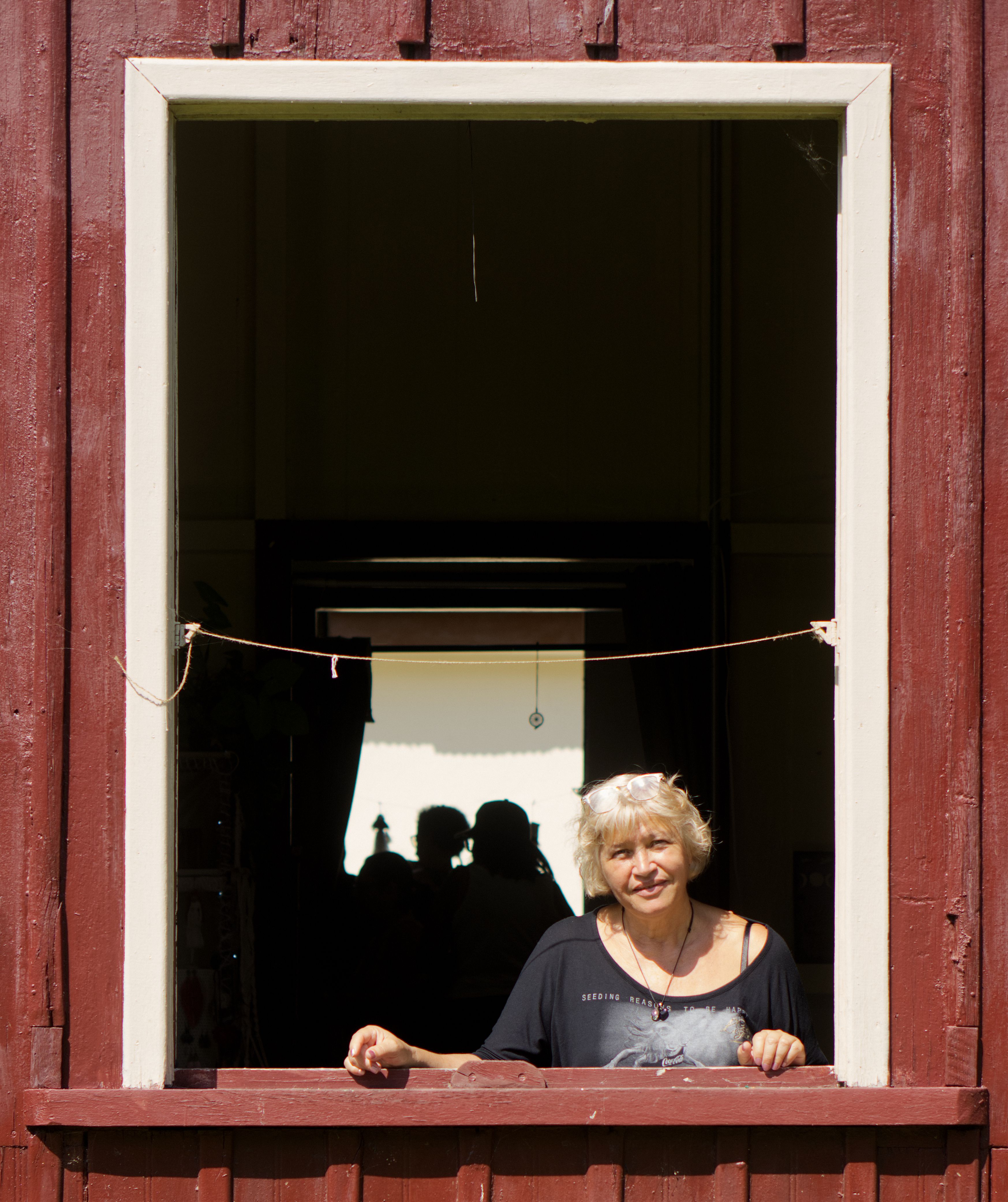 An elderly woman stands in a wooden window frame under bright daylight, São Paulo, Brazil.